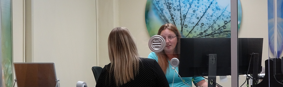 Two people speaking through a window with a speaker in an office.