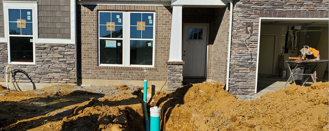 A newly built stone exterior home with dug up piles of dirt in the front lawn with blue and white underground pipes exposed.