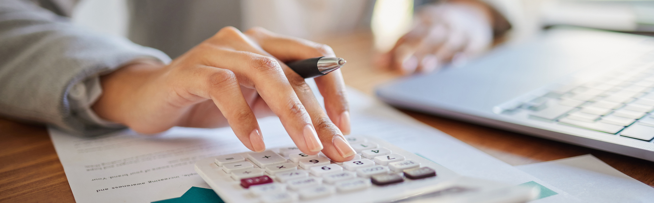 a person holding a pen and typing on a calculator while looking at their computer